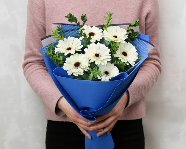 Букет із 7 білих міні гербер у стильній упаковці із зеленню