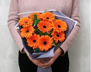 Букет з 9 помаранчевих міні гербер у стильній упаковці із зеленню