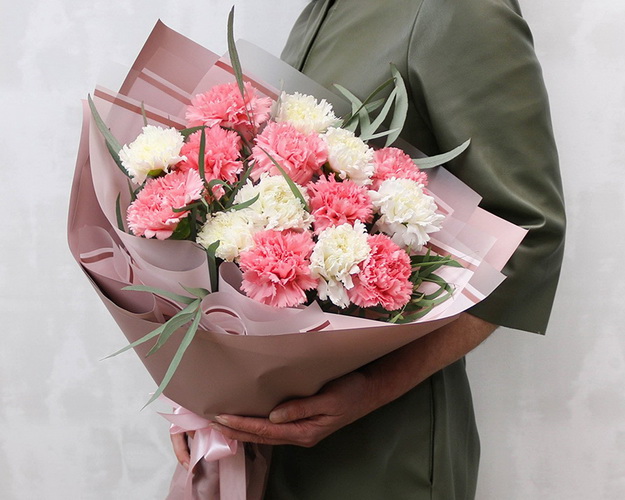 Букет із 15 рожевих та білих гвоздик у стильній упаковці із зеленню.