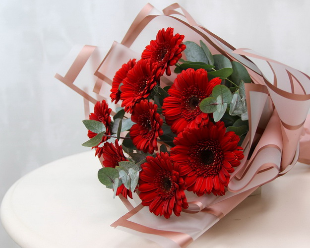 Букет із 9 червоних міні гербер у стильній упаковці із зеленню