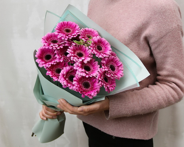 Букет із 15 малинових міні гербер у стильній упаковці із зеленню.