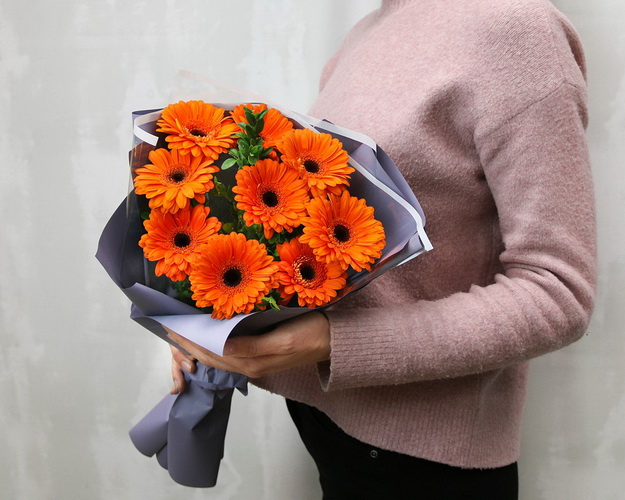 Букет з 9 помаранчевих міні гербер у стильній упаковці із зеленню