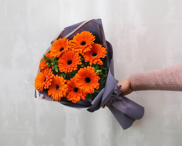 Букет з 9 помаранчевих міні гербер у стильній упаковці із зеленню