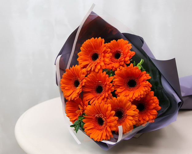 Букет з 9 помаранчевих міні гербер у стильній упаковці із зеленню