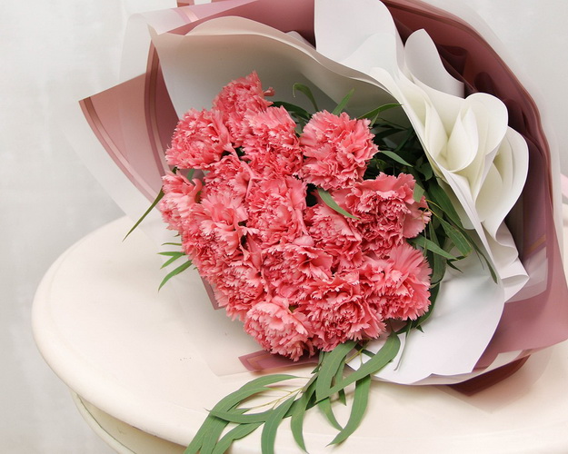 Букет із 15 рожевих гвоздик у стильній упаковці із зеленню