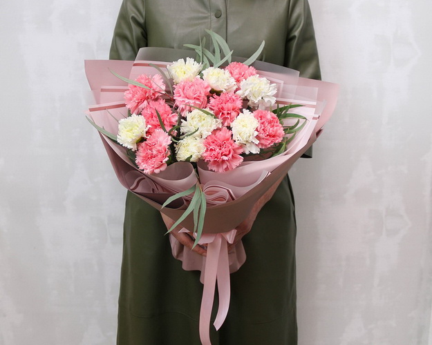 Букет із 15 рожевих та білих гвоздик у стильній упаковці із зеленню.