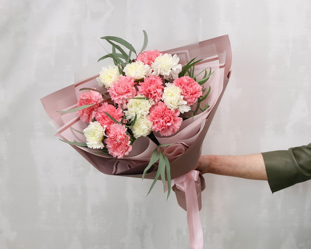 Букет із 15 рожевих та білих гвоздик у стильній упаковці із зеленню.