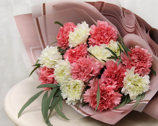 Букет із 15 рожевих та білих гвоздик у стильній упаковці із зеленню.
